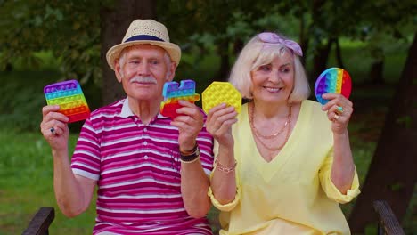 Smiling-senior-old-grandmother-grandfather-holding-anti-stress-touch-screen-push-pop-it-popular-toy