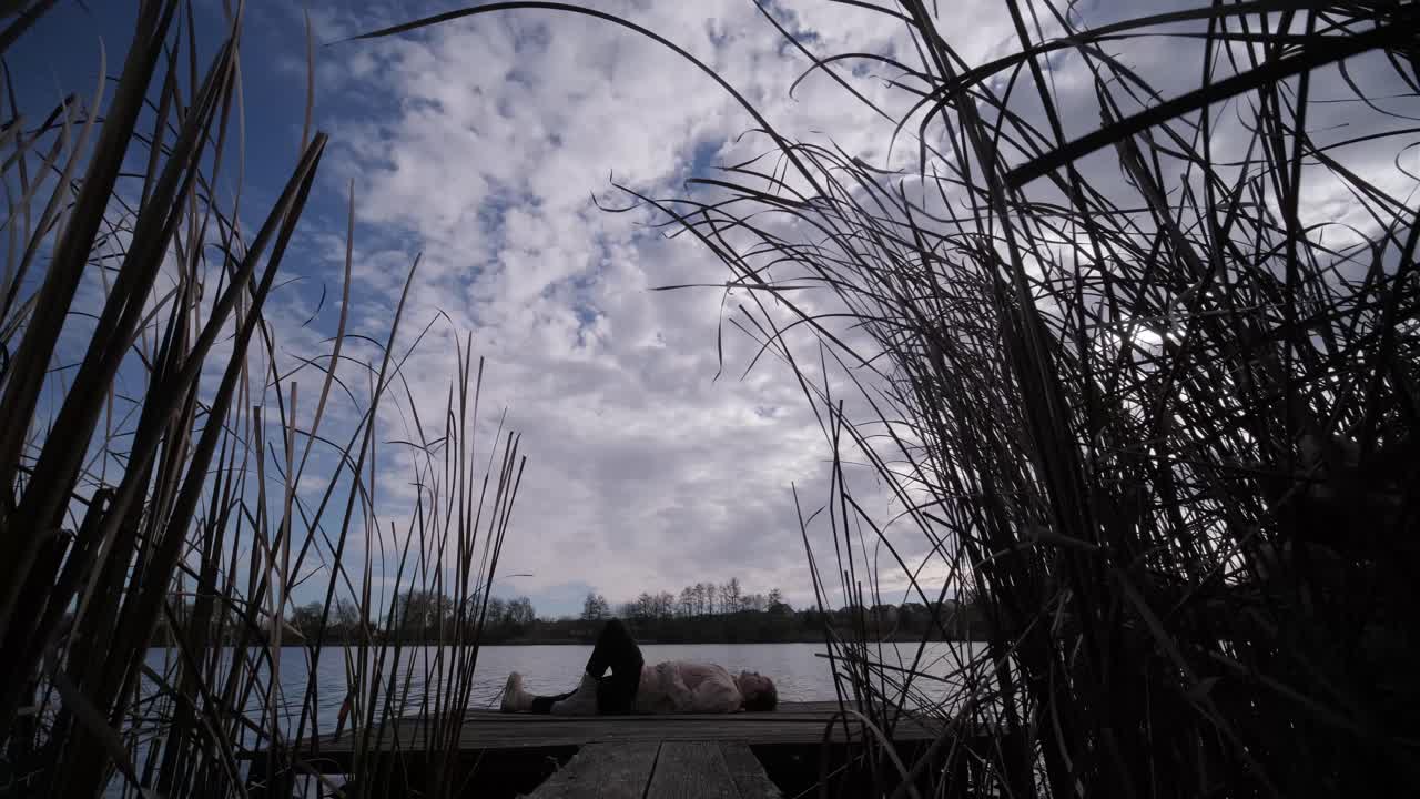 젊은이가 나무로 된 보행자 다리 위에 혼자 누워서 호수를 쳐다보고, 삶에 대해 생각하고, 자연에서 평화로운 분위기를 누리고, 신선한 공기를 즐기고, 뒤를 바라보고 있습니다.