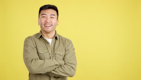 happy asian man with arms crossed on yellow background