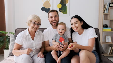 Glückliche-Familie,-Die-Zusammen-Auf-Dem-Sofa-Im-Wohnzimmer-Sitzt-Und-über-Videoanruf-Spricht