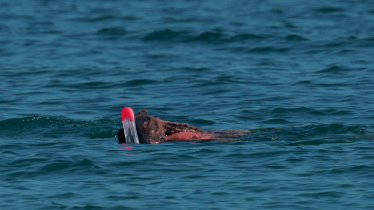 A swimmer wearing a full face snorkel mask floats and explores the calm turquoise sea