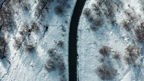 Aerial-view-of-a-snow-covered-landscape-with-a-winding-road-cutting-through-bare-trees