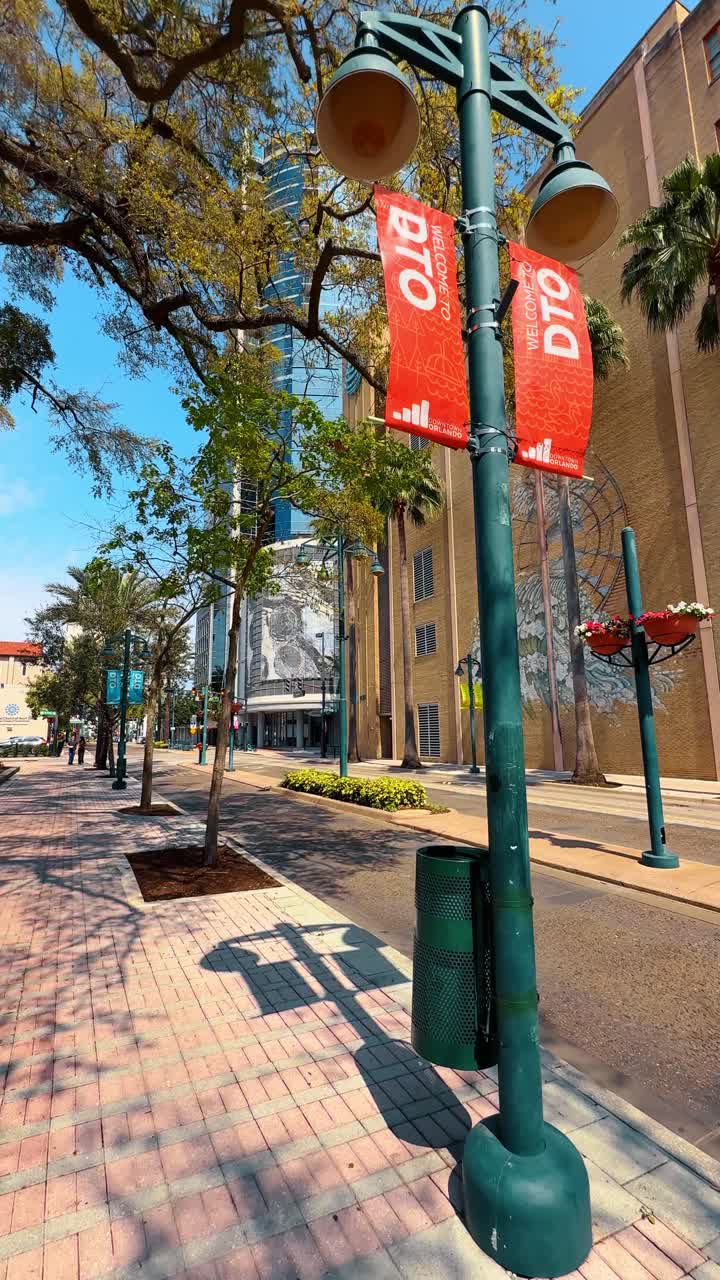 Orlando, USA, 9 czerwca 2025: Scena uliczna z centrum Orlando z zieloną latarnią uliczną i muralem. Szerokokątny widok chodnika miejskiego z banerami DTO i kolorową sztuką ścienną na Florydzie.