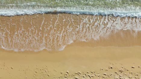 olas rodando en una playa de arena dorada, vista aérea de arriba hacia abajo