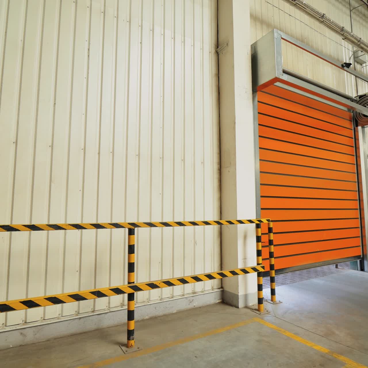 automatic roller gates of orange color are lowering down in the warehouse of woodworking plant. Camera movement to the right