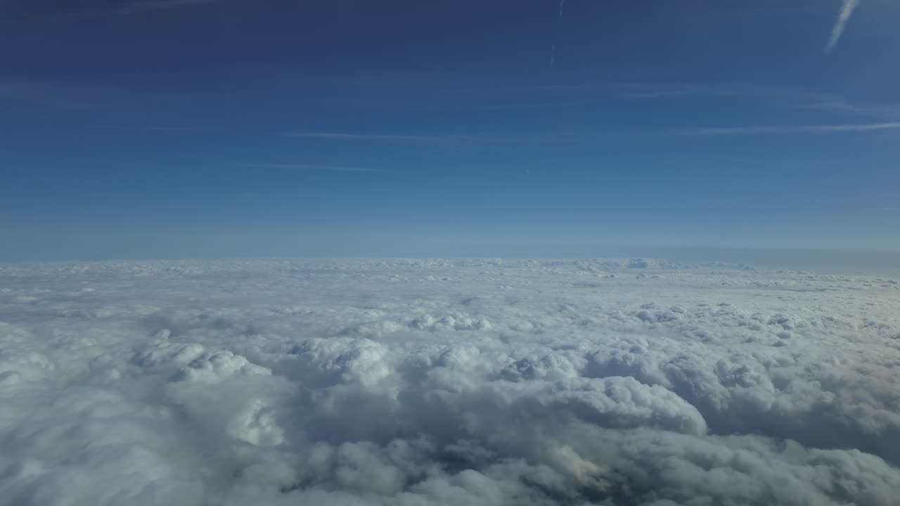 An aerial view from inside a jet airplane flying at supersonic speed over an endless sea of stratus clouds under a blue sky.