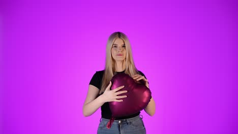 cute woman looking at camera and holds red balloon heart, purple background