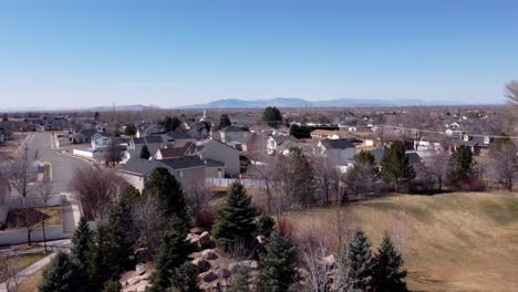 Drone-flying-backwards-and-up-a-dead-tree,-revealing-a-children’s-public-rock-park-and-suburban-middle-class-American-neighborhood-on-a-sunny-spring-day