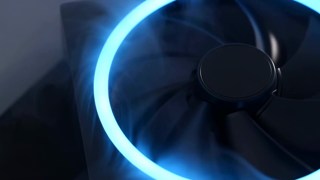 Rotating black fan blades remain centered beside a bright cyan-blue light ring while faint drifting haze crosses dark enclosure, creating detailed close-up of active cooling.