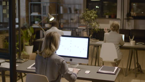 rear view of woman employee observing stadistics and graphics on computer monitor sitting at desk in the office