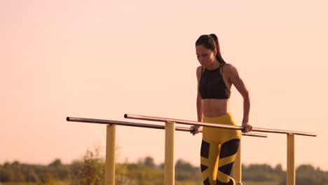 schöne, schlanke sportlerin in schwarzem oberteil und gelber hose bei sonnenuntergang führt in slowmotion liegestütze auf einer parallelen horizontalen stange durch.