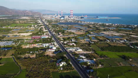 aerial view of vietnamese coastline highway traffic road, industrial power plant station at distance and agricultural rice fields in ninh thuan