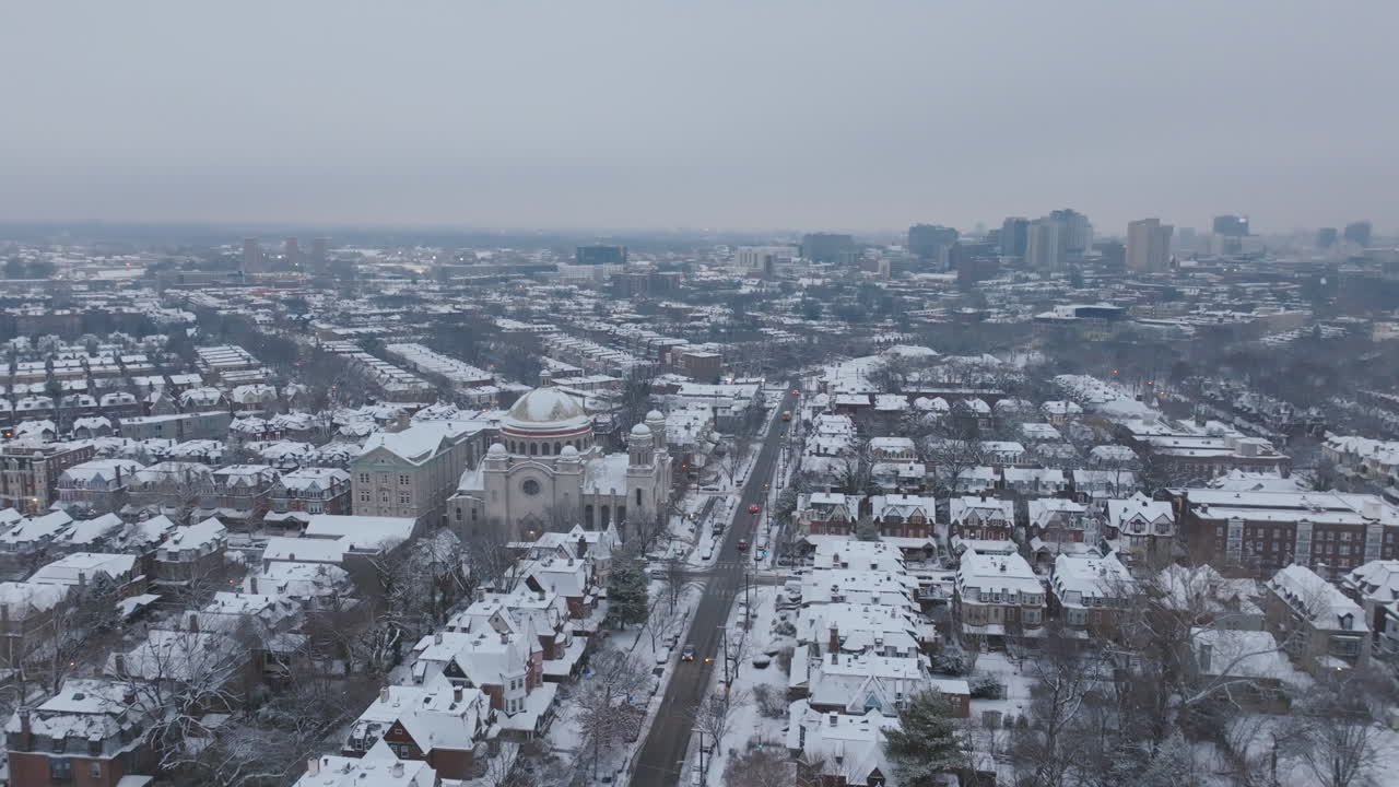 Aerial footage rotating around St. Francis De Sales Catholic Church in snow covered neighborhoods in West Philadelphia, Pennsylvania with downtown in the background.