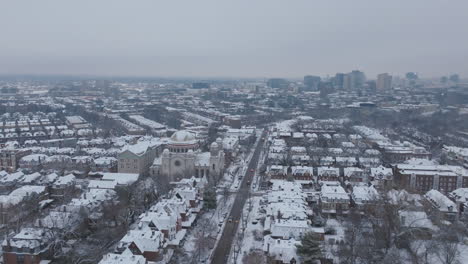 aerial footage rotating around st. francis de sales catholic church in snow covered neighborhoods in west philadelphia, pennsylvania with downtown in the background.