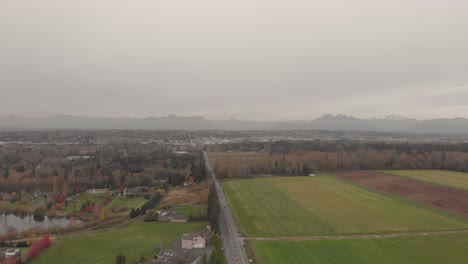 Drone-4K-Footage-of-agricultural-grassfields-farmland-near-a-thick-wooded-forest-in-a-rural-develop-environment-by-a-roadside-Langley-BC