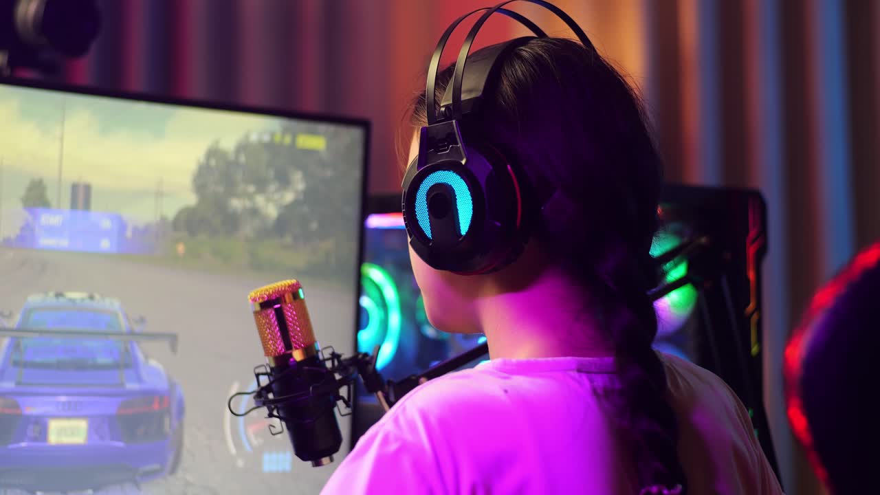 vista de atrás de una chica asiática que se estira mientras juega a un juego de carreras de coches a través de la red en una computadora personal. videojuego de transmisión en vivo, escritorio iluminado por luz de tira de led rgb