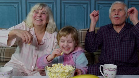 grandparents watching cartoons movies on tv television with granddaughter at home, happy laughing