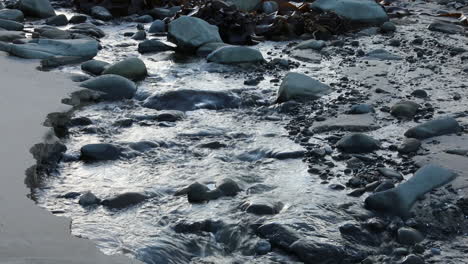 Inland-river-running-into-open-sea-water-with-seaweed-next-to-sandy-beach