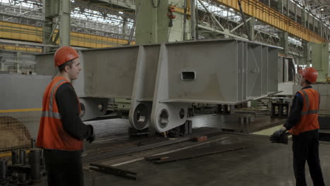 industrial workers handling heavy metal components in a factory