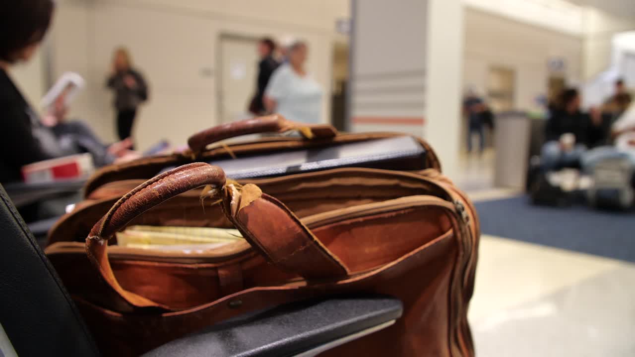 4k Man's brown leather briefcase bag sitting in chair waiting to board flight or bus for travel