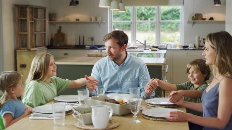 family sitting around table at home joining hands and saying grace before meal