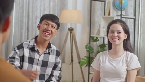 아시안 소년과 소녀가 집에서 친구들과 토론하는 동안 미소 짓고 엄지손가락을 카메라에 보여주고 있습니다.