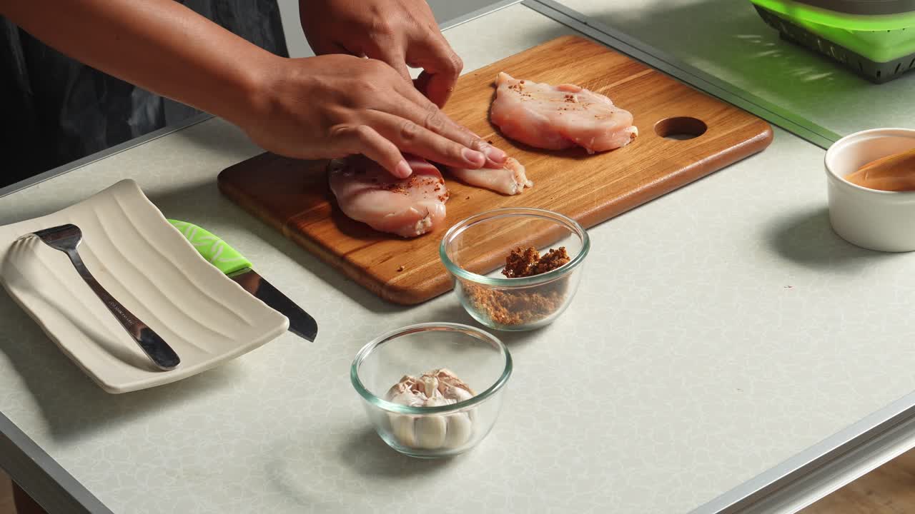 Mani che condiscono pollo crudo per la cottura