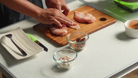 hands seasoning raw chicken breast for cooking