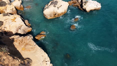 Aerial-top-down-of-rocks-and-waves-of-Atlantic-ocean-in-Portugal-lighting-by-sun---tilt-down