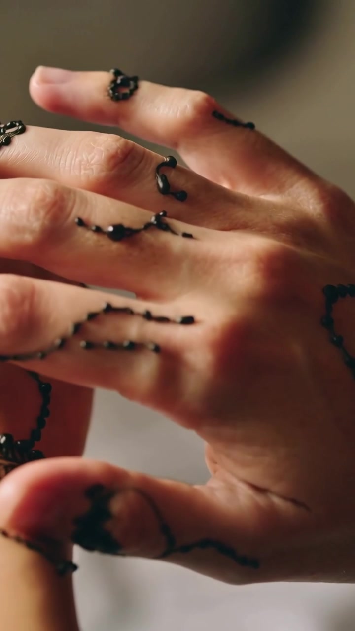 Vertikales Video: Nahaufnahme von Händen, die schwarze Paste im Raum anheben und Perlen mit einem geflochtenen Armband formen.