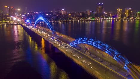 Impresionante-Y-Colorido-Lapso-Nocturno-Aéreo-Del-Icónico-Puente-Del-Dragón-Cau-Rong,-El-Tráfico-Y-El-Horizonte-De-La-Ciudad-Cambian-De-Color-En-Danang,-Vietnam