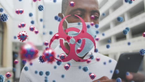 animation of covid 19 cells and biohazard symbol over man in face mask using smartphone