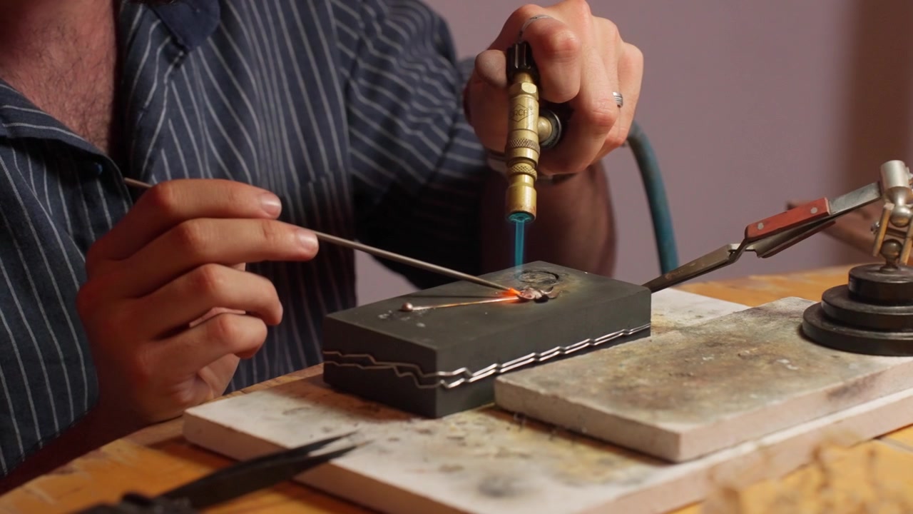 An artisan focuses on welding metal with a torch, showing expertise in jewelry making.