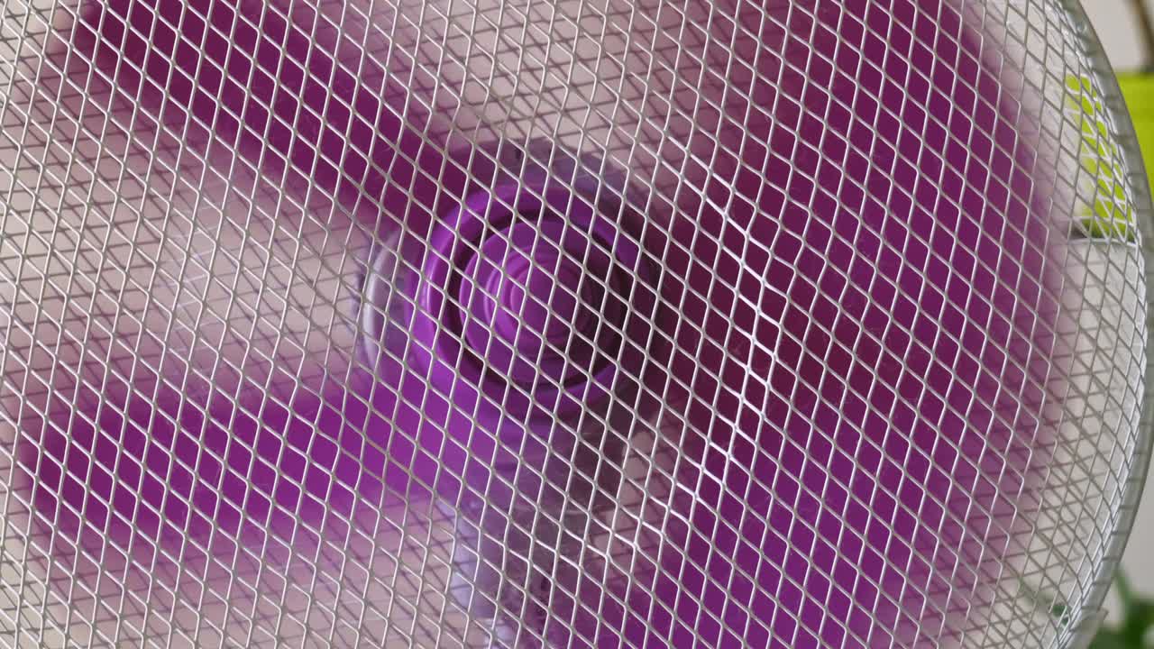 aparato doméstico ventilador eléctrico aspas de plástico giratorias detrás de malla de seguridad de alambre que circula el aire en la habitación cerrar deslizamiento lento a la izquierda