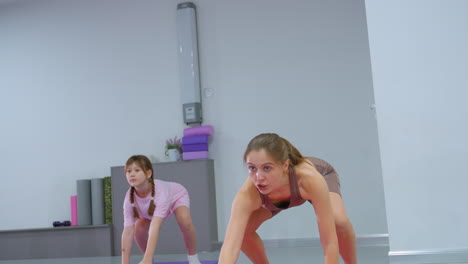 instructor guides niece through a squat workout session, assisting as she gradually prepares for push-ups, focus on strength, endurance, and proper form in a bright, professional fitness environment