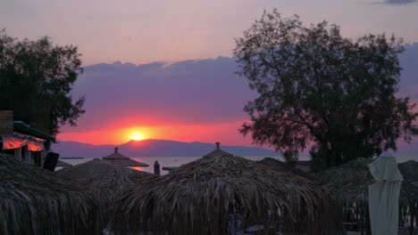 hermosa puesta de sol en la isla agkistri, argosaronikos, grecia, con sombrillas naturales hechas de heno en primer plano