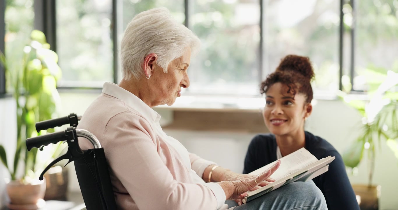 Young Caregiver Reading a Book to an Elderly Woman in a Wheelchair