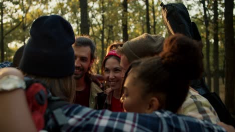 a-happy-group-of-friends-in-hiking-clothes-hugging-in-a-circle-and-enjoying-their-company.-A-small-group-rejoices-while-hiking-in-the-summer-forest