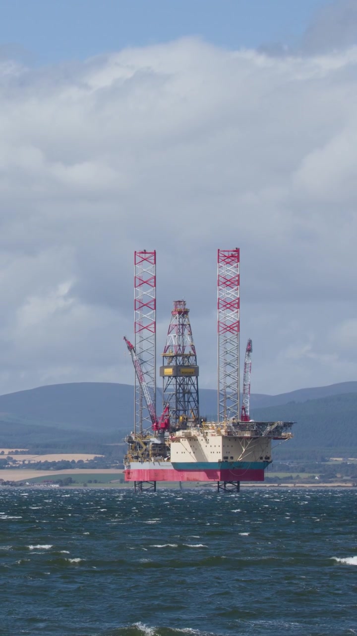 Offshore olieplatform står i oprørt hav, fjerne bakker, dagslys, vidvinkeloptagelse, let kamerabevægelse