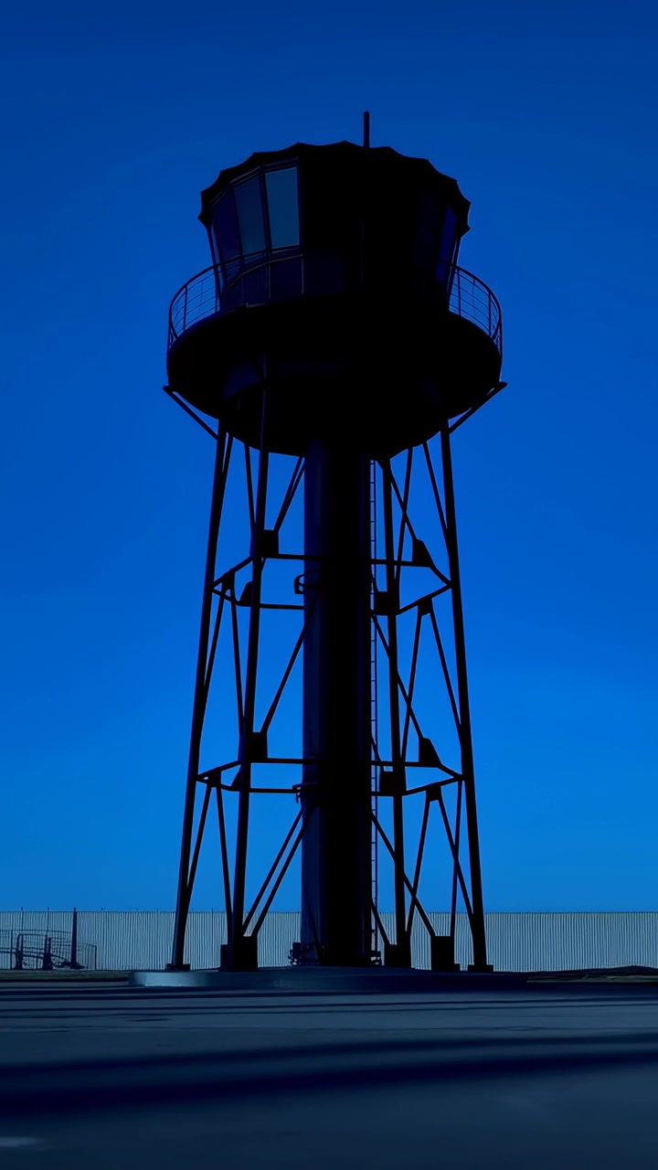 Video verticale: Luce solare mutevole che fa sì che una torre proietti lunghe ombre su un tetto piatto, con cabina circolare