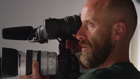 male film camera operator taking camera off tripod to shoot handheld movie or video in studio