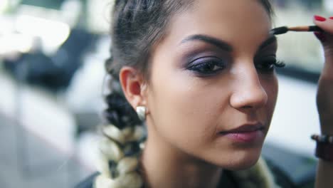 vista de cerca de una joven sentada en el estudio de belleza mientras el maquillador corrige las cejas usando un cepillo especial