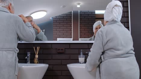 Senior-couple-grandmother-and-grandfather-brushing-teeth-and-looking-into-a-mirror-at-bathroom