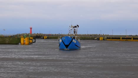 blue fishing boat enters harbor in kolobrzeg, poland