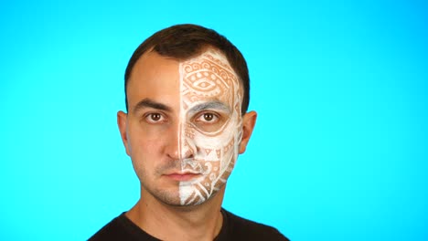 hombre con cara pintada se vuelve y mira a la cámara contra un fondo azul