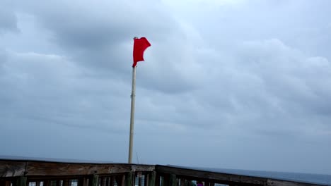 a red flag flies on a pier in the wind indicating dangerous surf at the beach in florida