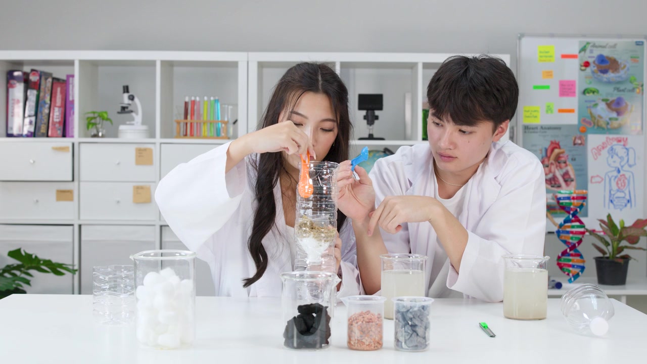 과학 수업 중에 실험복을 입은 두 학생이 플라스틱 병 정수기를 조립한다.