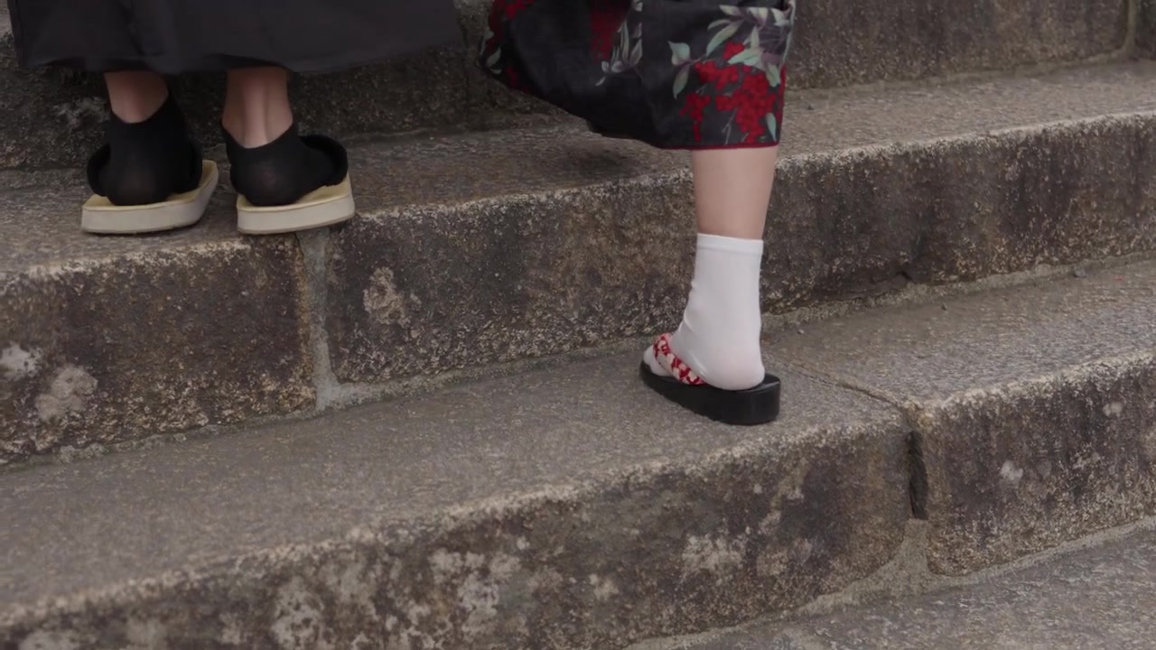 Feet in white tabi socks and traditional sandals walking up weathered mossy stone steps