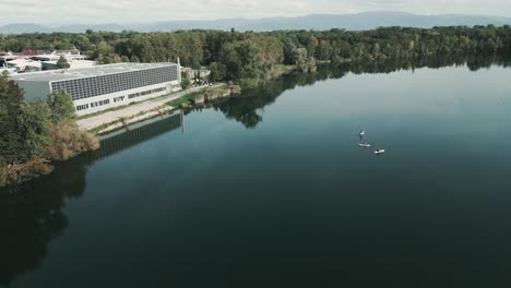 el dron vuela diagonalmente sobre un hermoso lago en alemania con los remeros de pie en el medio y los árboles a la vista.