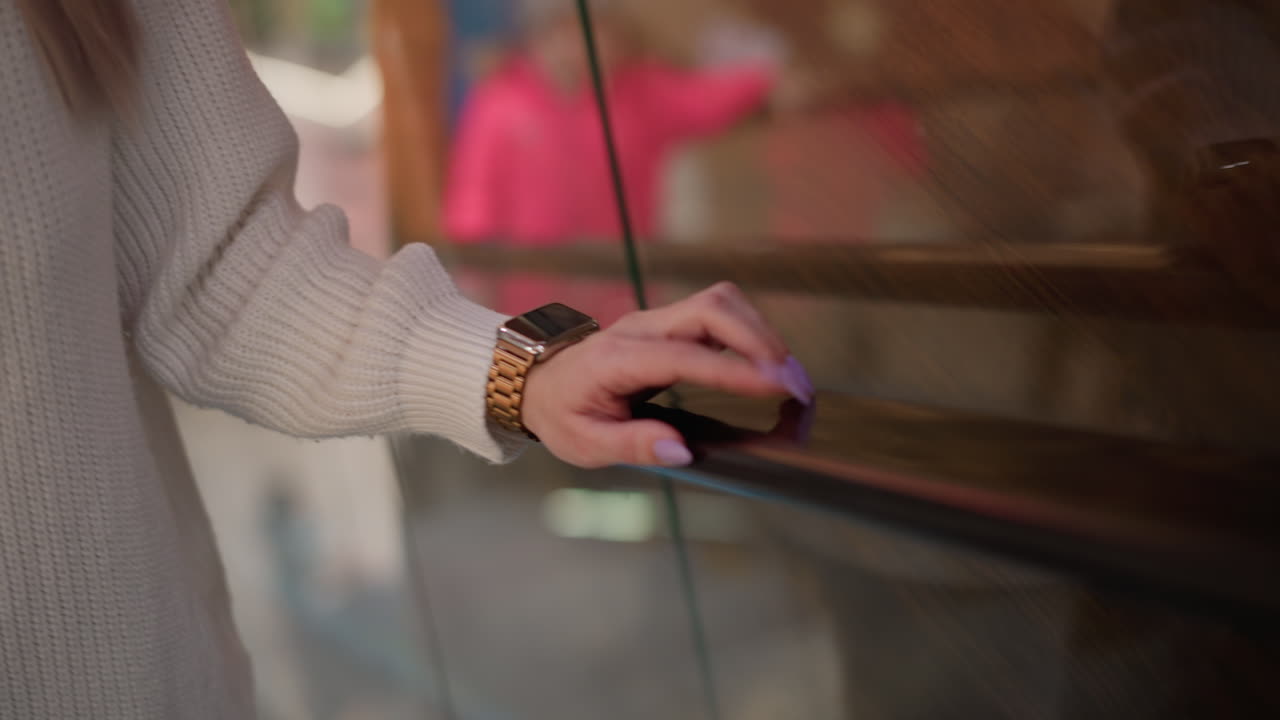 close up view of moving walkway metal handrail being tapped by elegant lady wearing gold wrist watch and manicured nails in modern mall setting, highlighting smooth black railing surface